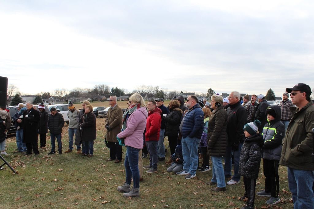 A crowd of people standing outdoors, listening. Cloudy day.