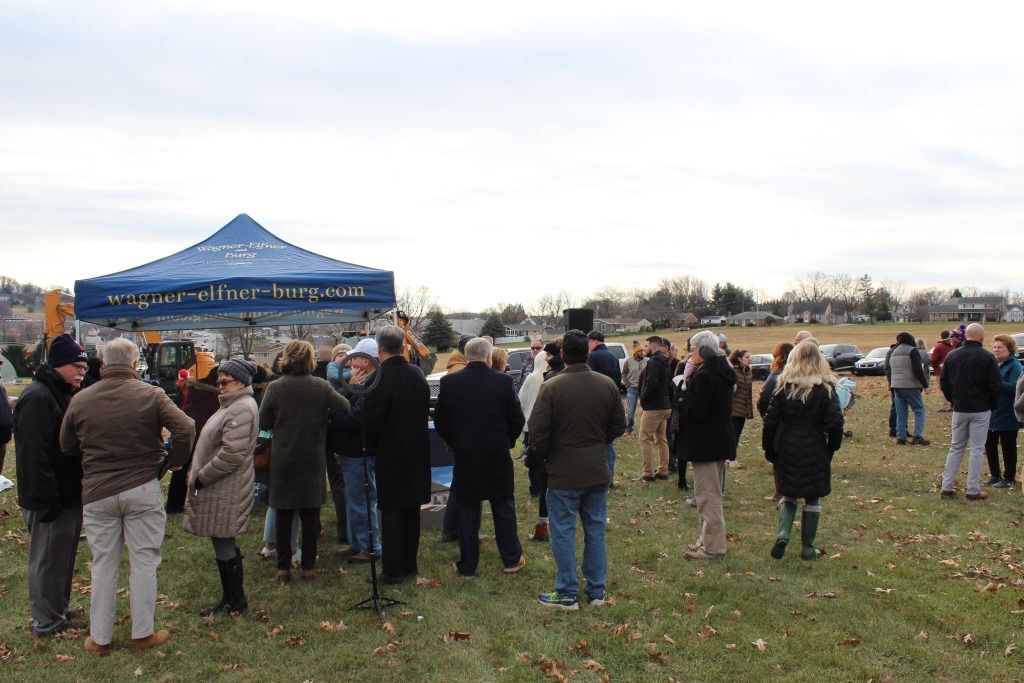 Group of people gathered outdoors under a blue tent; overcast sky, field setting.