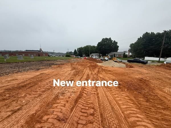 New entrance construction site with brown dirt road and heavy equipment, under a cloudy sky.