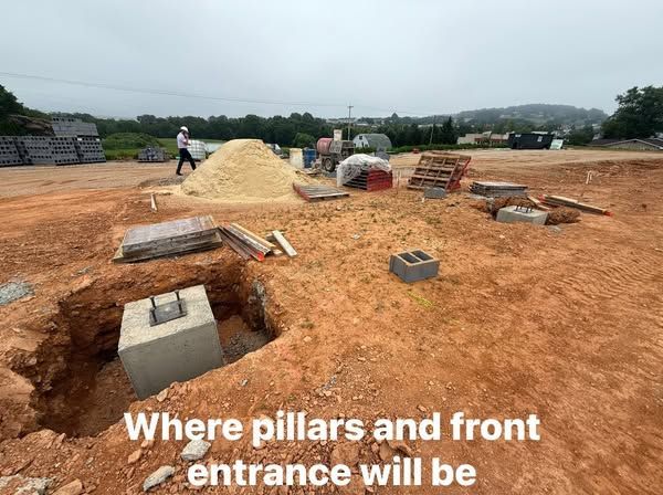 Construction site with excavated holes, concrete pillars, and materials; location of pillars and entrance indicated.