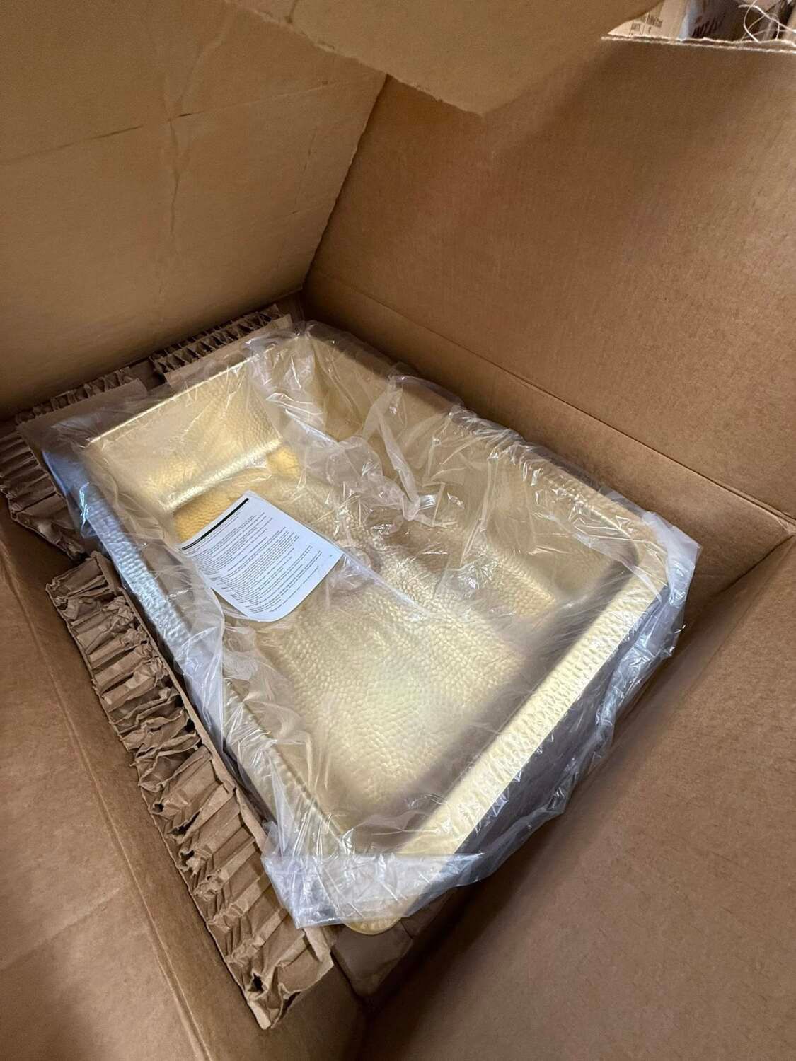 Gold-colored rectangular sink in a cardboard box, wrapped in plastic.