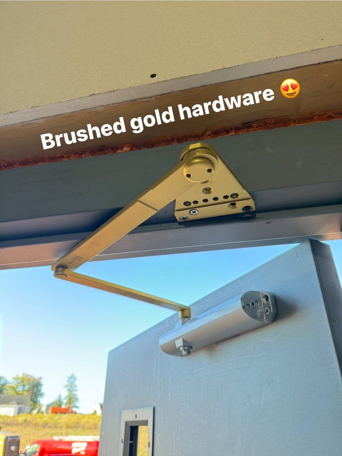 Brushed gold door closer hardware installed on a gray door.