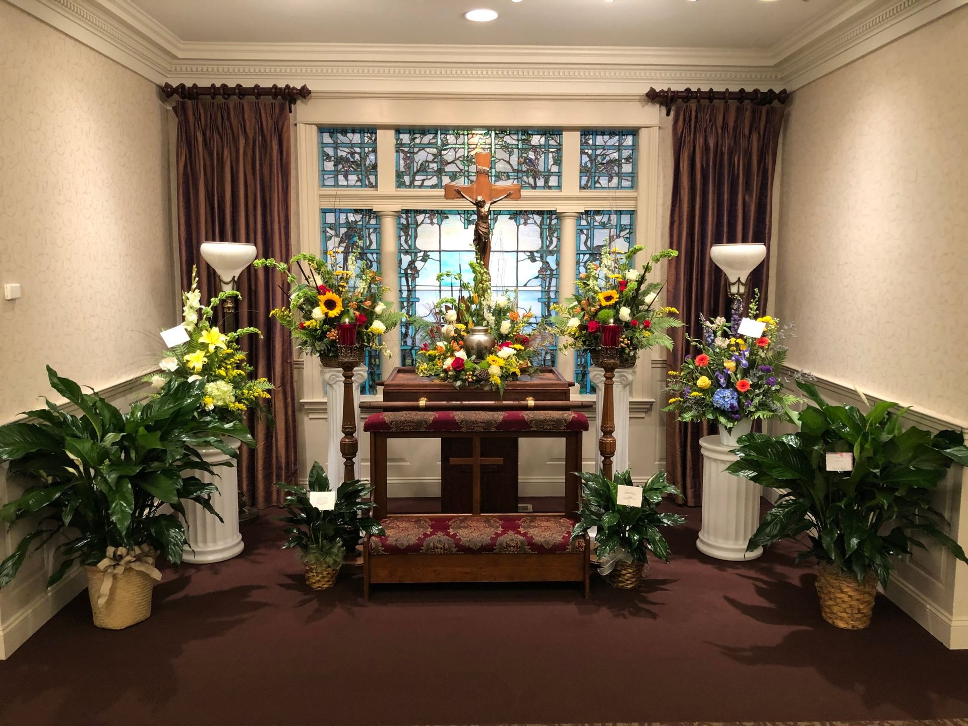 A group of people are standing around a wooden urn surrounded by red roses at a funeral.
