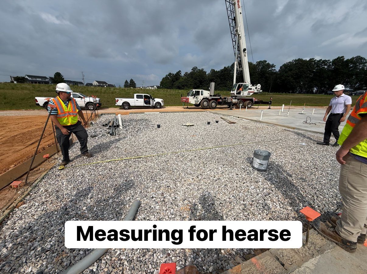 Construction workers measuring on a gravel surface. A crane is in the background. Cloudy sky.