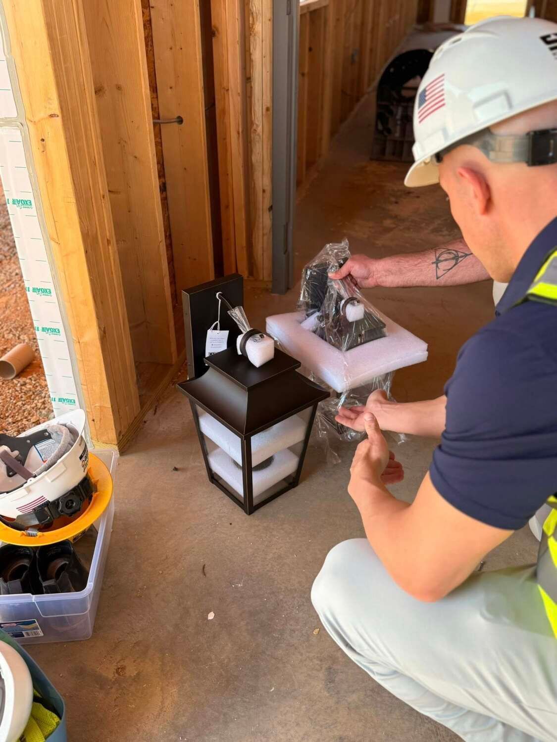 Person holding two black outdoor lights near an unfinished wall on a construction site.