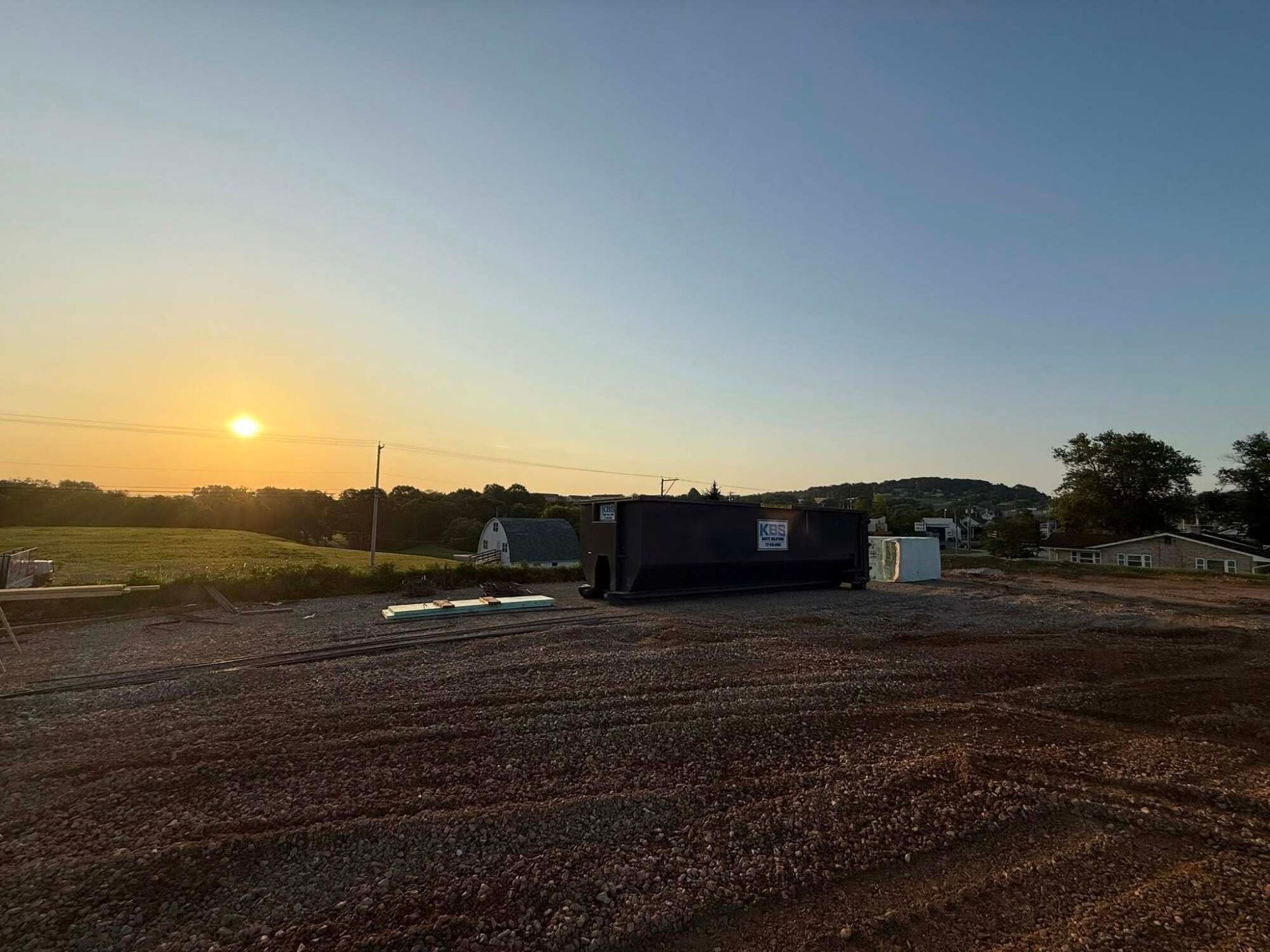 Sunset over a construction site with a dark rectangular container in the center and gravel ground.