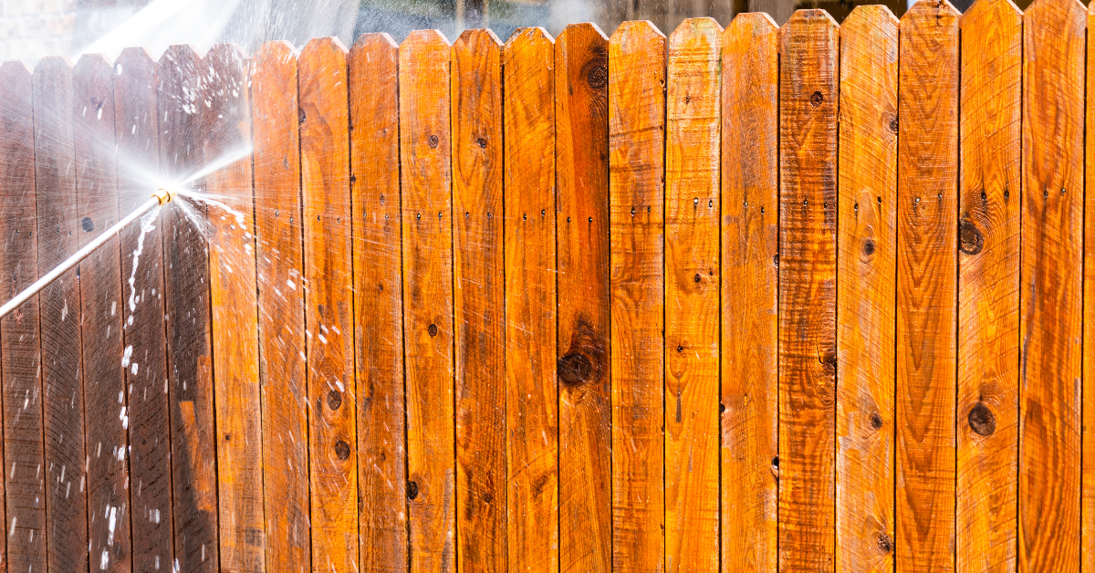 A wooden fence is being cleaned with a high pressure washer.