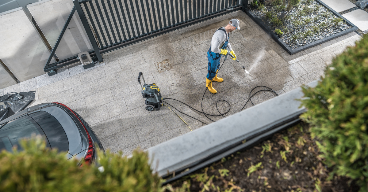A man is cleaning a driveway with a high pressure washer.