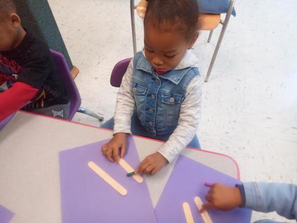 A little girl is sitting at a table playing with popsicle sticks