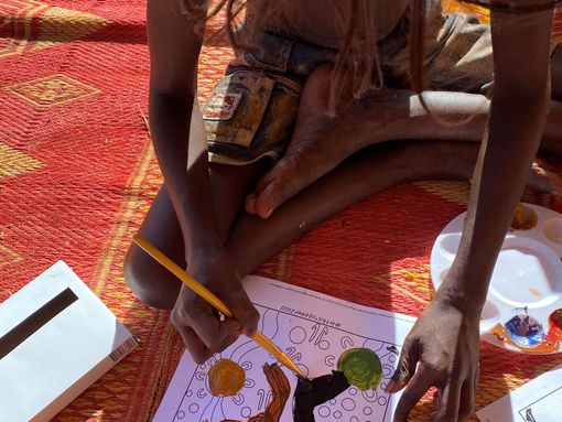 A child is sitting on the floor drawing with a pencil