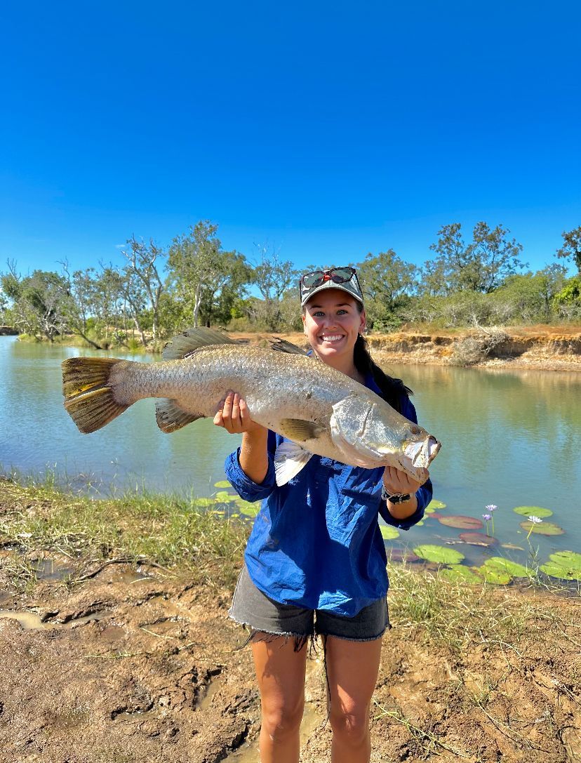 A woman is holding a large fish in her hands in front of a body of water.