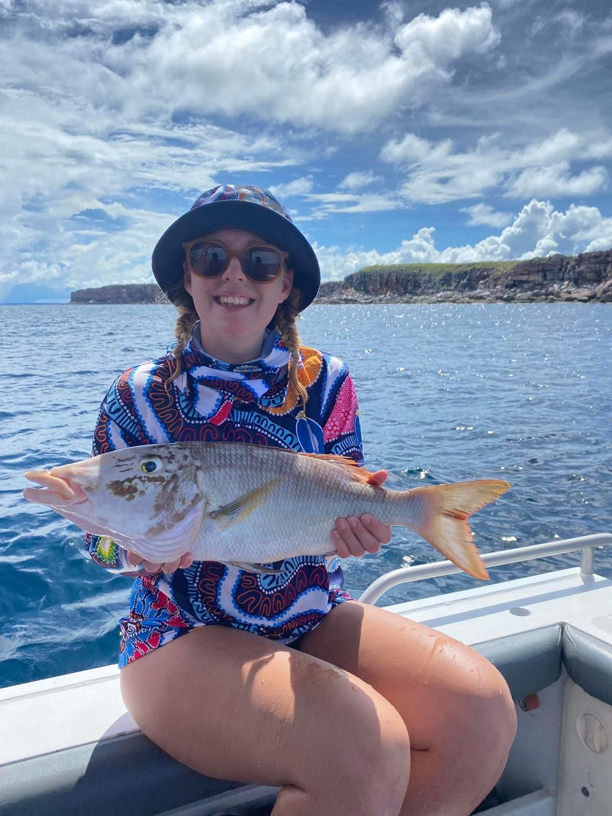 A woman is sitting on a boat holding a large fish.