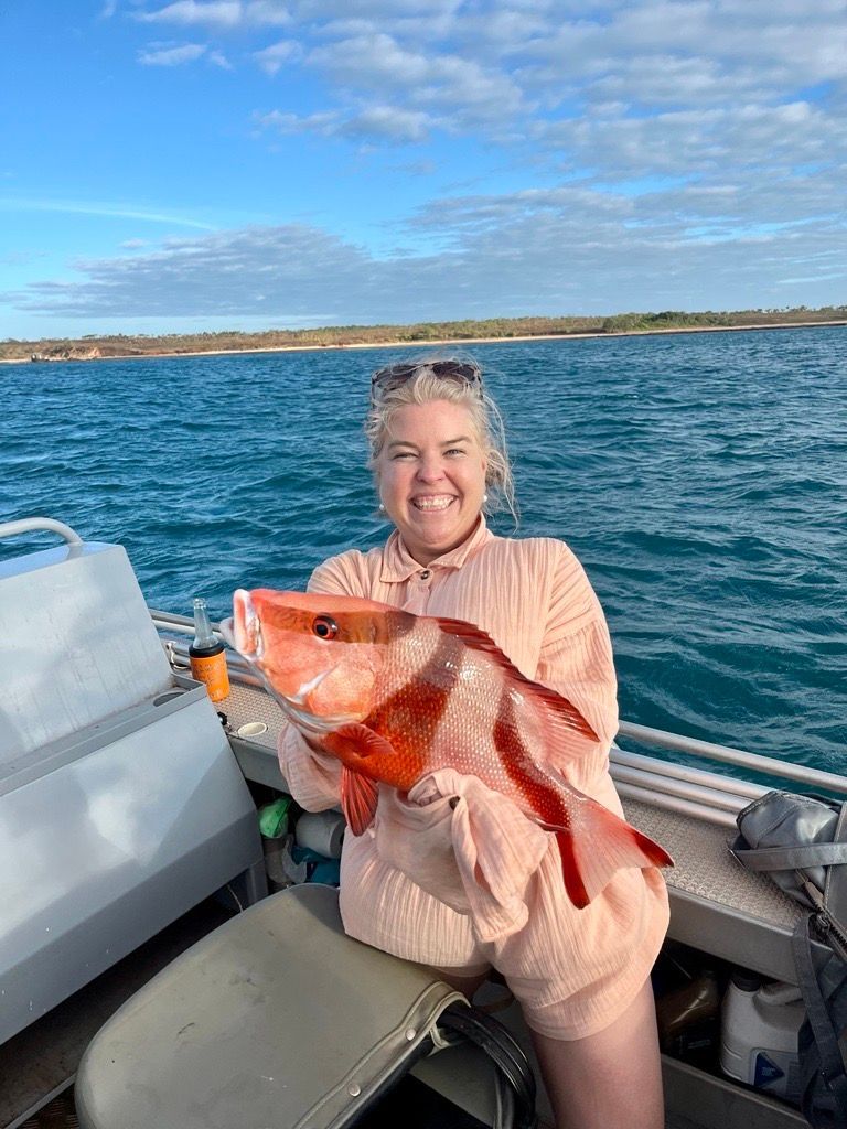 A woman is sitting on a boat holding a large fish.