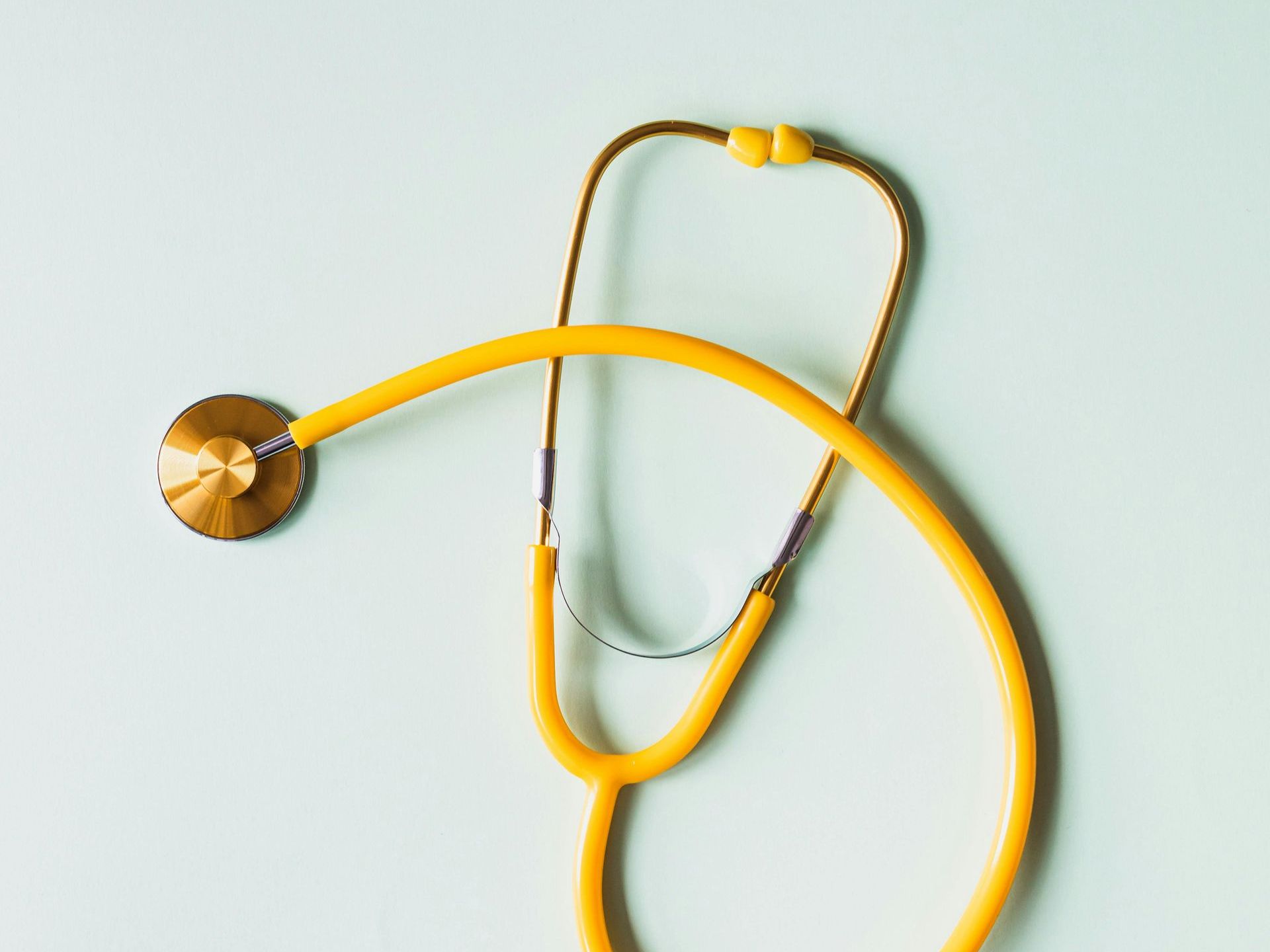 A yellow stethoscope is hanging on a white wall.