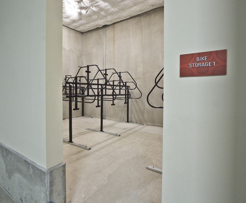 An empty bike storage room with metal racks, a concrete floor and walls, and a sign on the wall reading