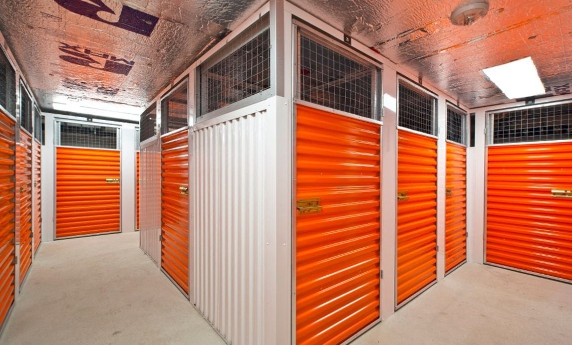 Indoor storage lockers with bright orange roll-up doors in a hallway.