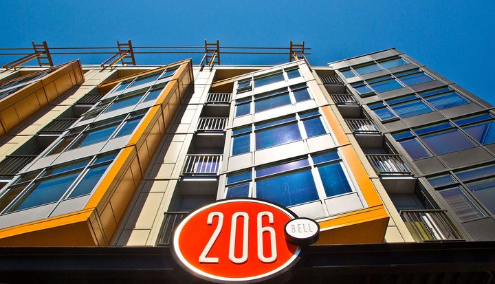 Low-angle view of a modern apartment building with bright yellow accents and a prominent red circular sign reading