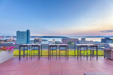 Rooftop terrace with bar-height stools and railing, overlooking city skyline and water.