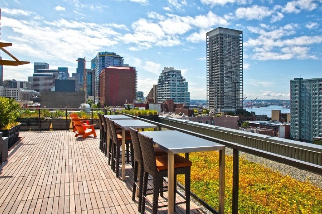 Rooftop terrace with long high tables, chairs, and a city skyline backdrop.