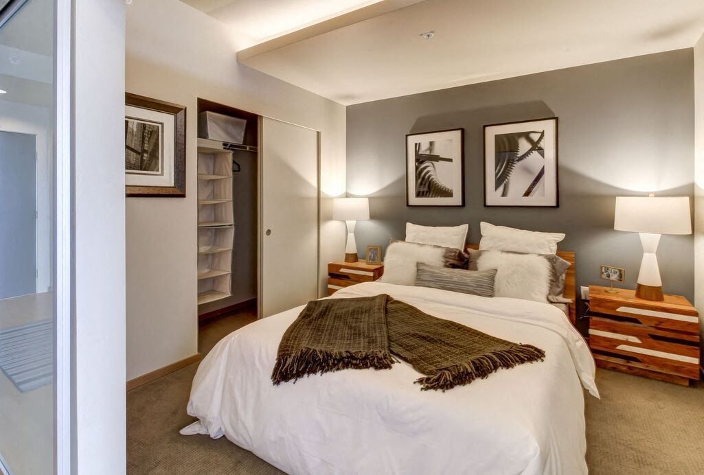 Bedroom with white bedding, two wooden nightstands, lamps, and gray accent wall.
