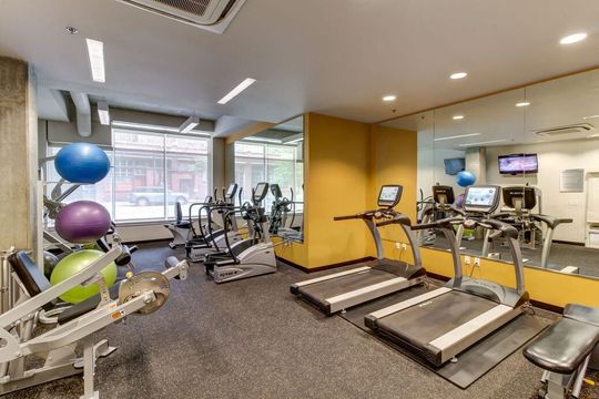Well-lit apartment gym with treadmills, bikes, weights, and a mirrored wall.