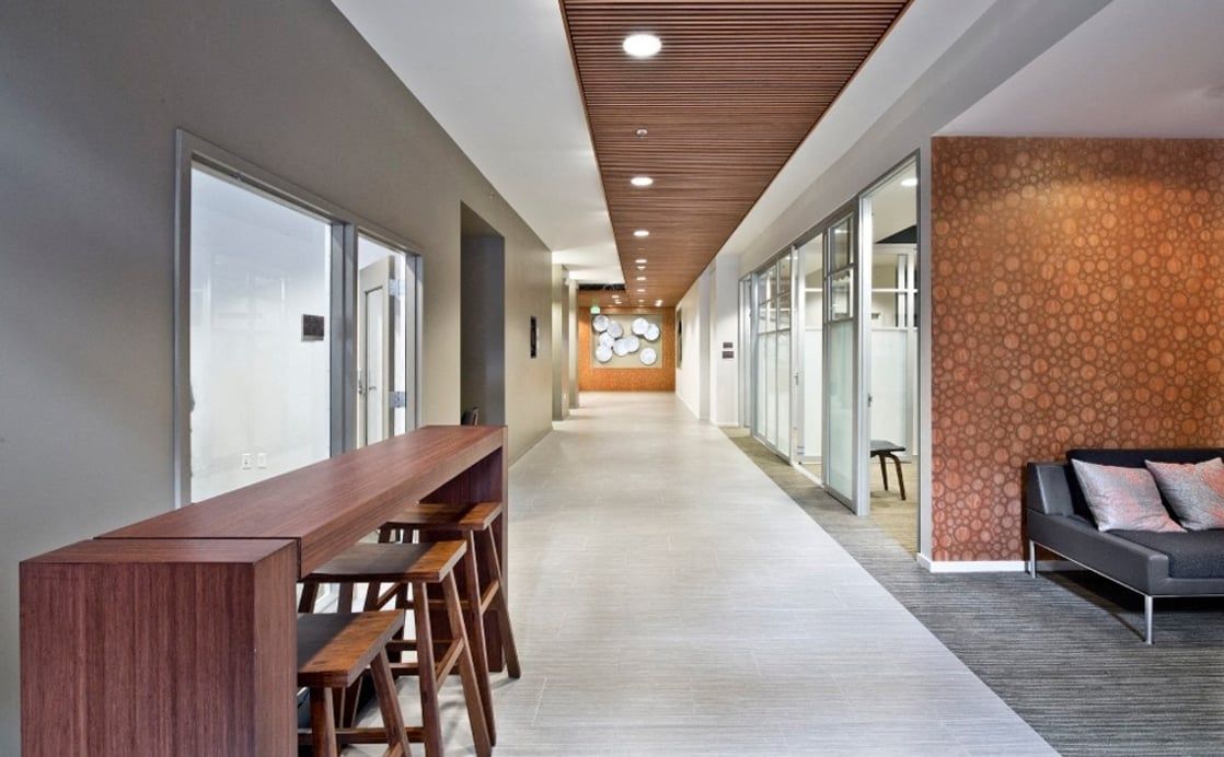 Interior hallway in a modern apartment building with glass-walled offices and a wood-topped bar.