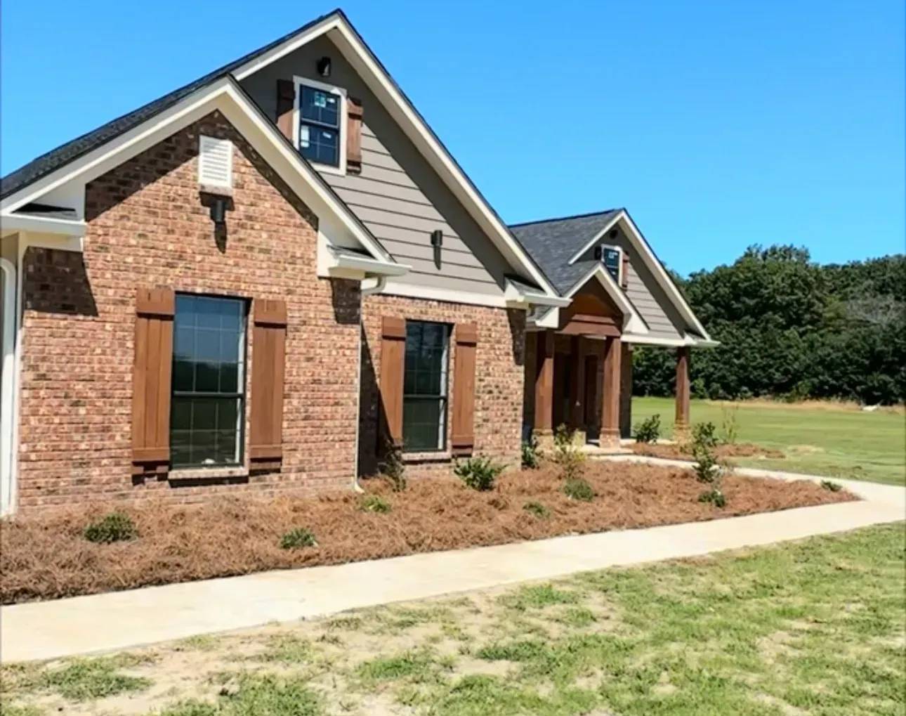 Brick house with brown shutters, tan siding, and a walkway on a sunny day.