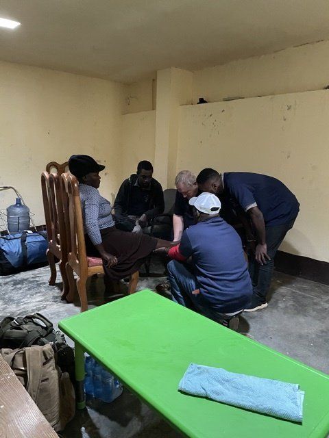 People assisting someone's foot. Indoors, one person sits, others stand/kneel around.