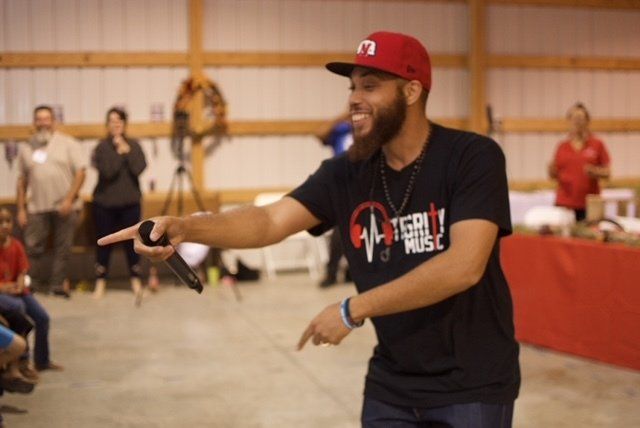Man in red cap and black shirt with microphone, gesturing at an event.