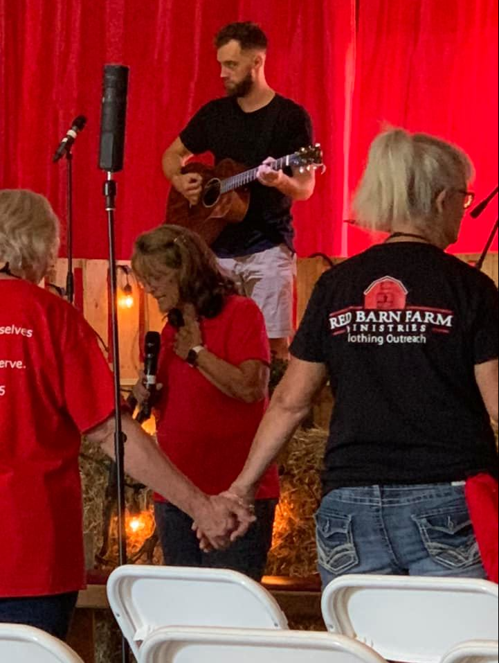 Man plays guitar on stage as people hold hands. Red backdrop.