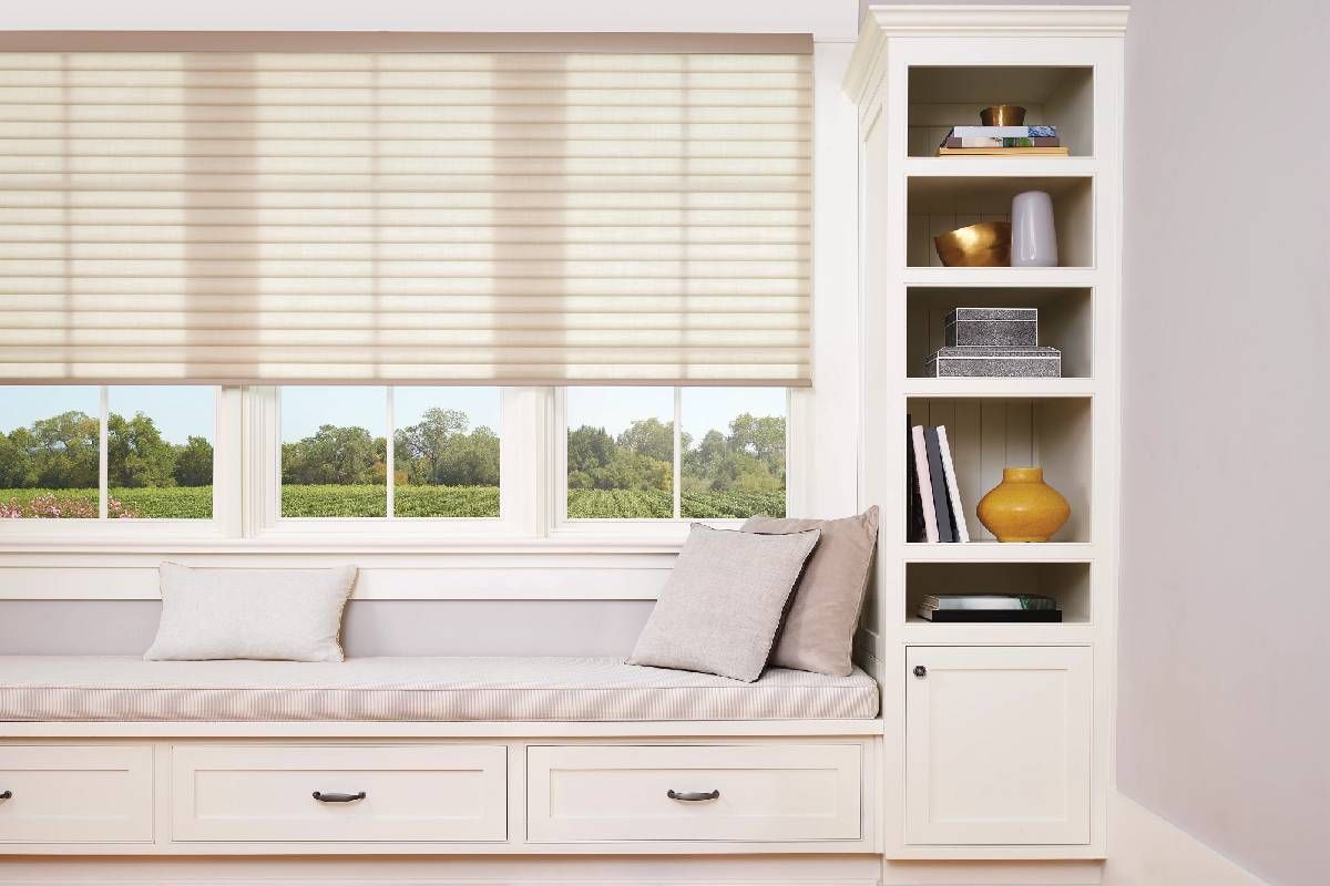 A living room with a window seat and a bookshelf with windows that have custom honeycomb shades