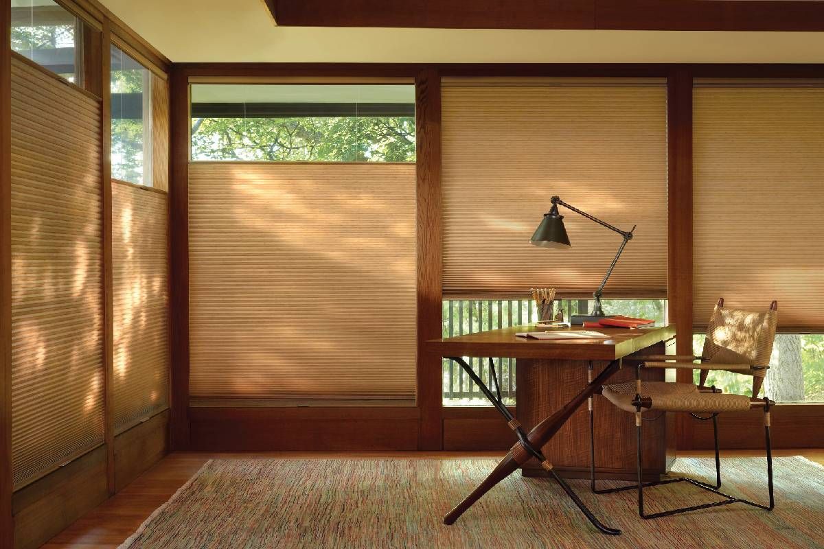 There is a desk and chair in the room with a lamp on it with windows that have custom honeycomb shades