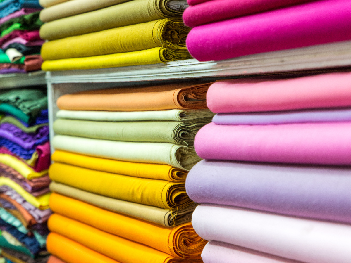 A bunch of colorful fabrics are stacked on top of each other on a shelf in a store.