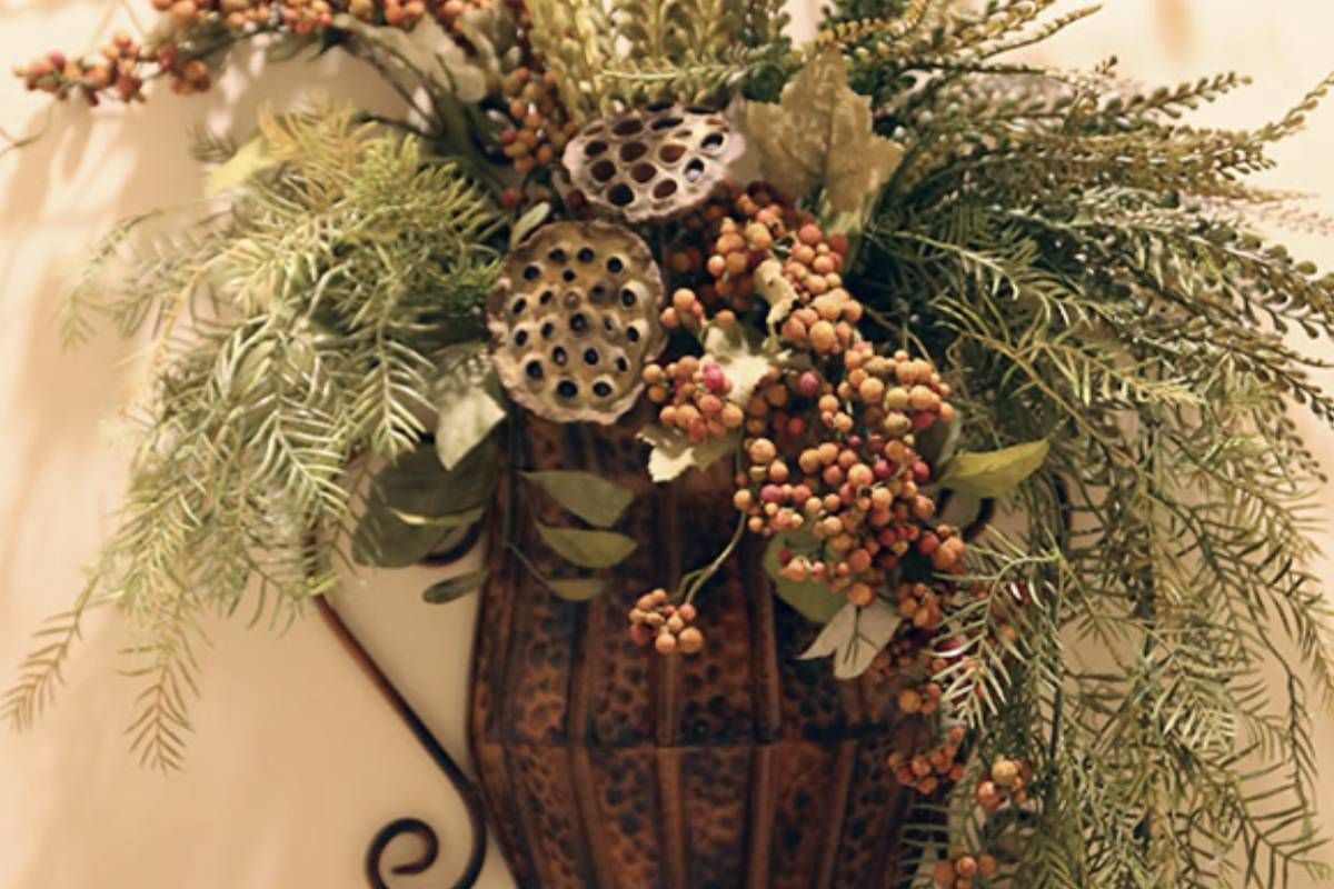 Home decorated with a vase filled with flowers and leaves is hanging on a wall.