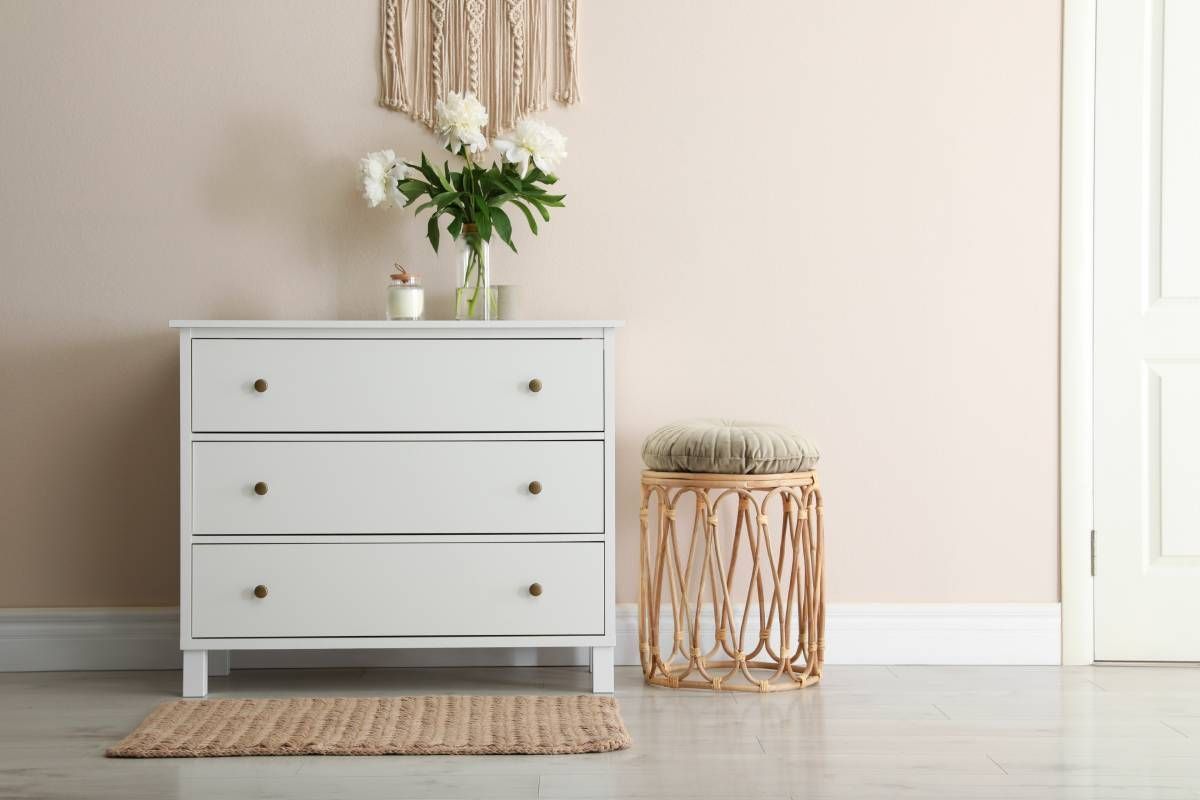 A white custom dresser with a vase of flowers on top of it in a room.