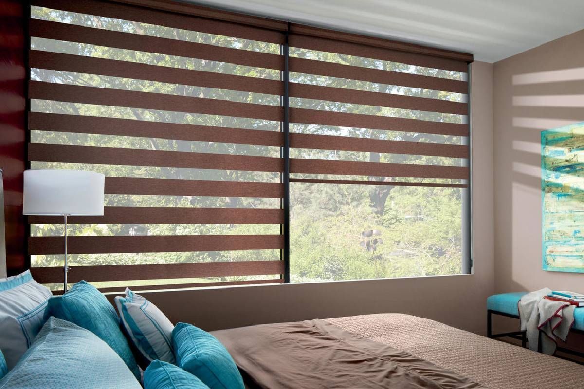 A bedroom with a bed , a lamp , and a large window with custom roller shades