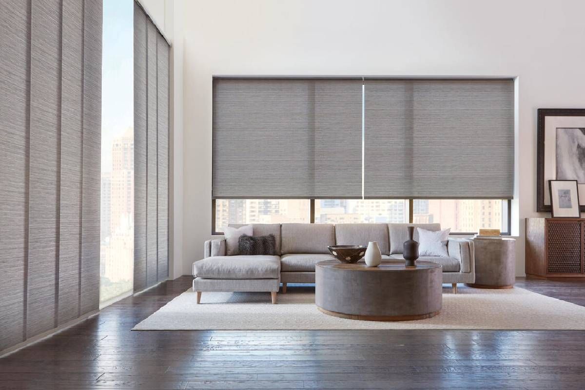 A living room with a couch , coffee table , and Hunter Douglass roller shades on the windows.