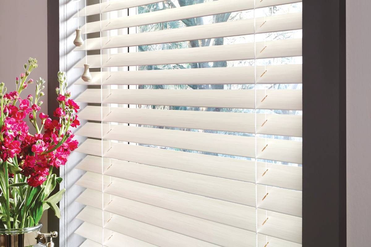 A window with Parkland wood blinds and a vase of flowers in front of it.