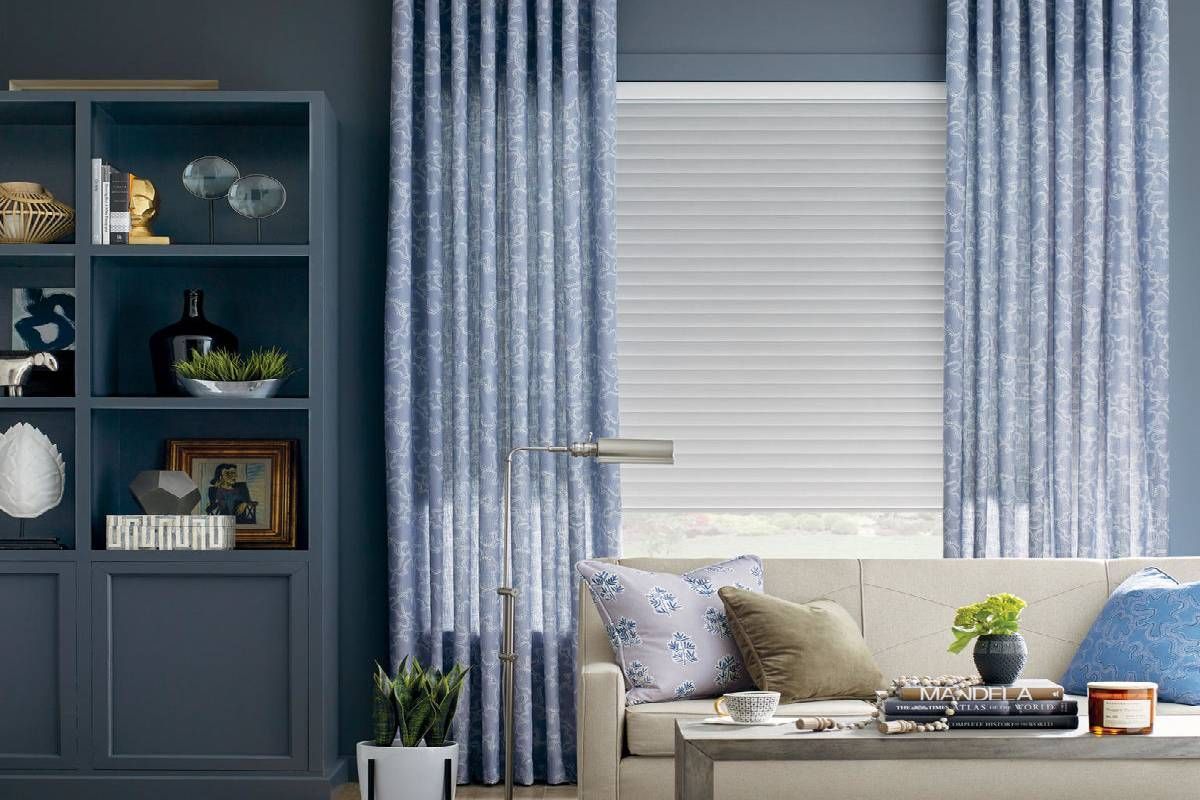 A living room with a couch , bookshelf , and blue curtains.