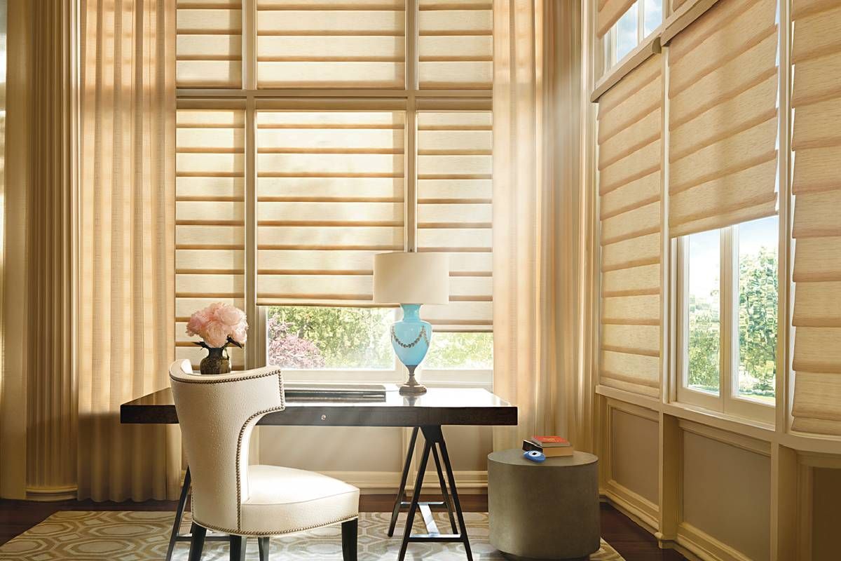 A room with a desk , chair , lamp and motorized treated windows by Hunter Douglas