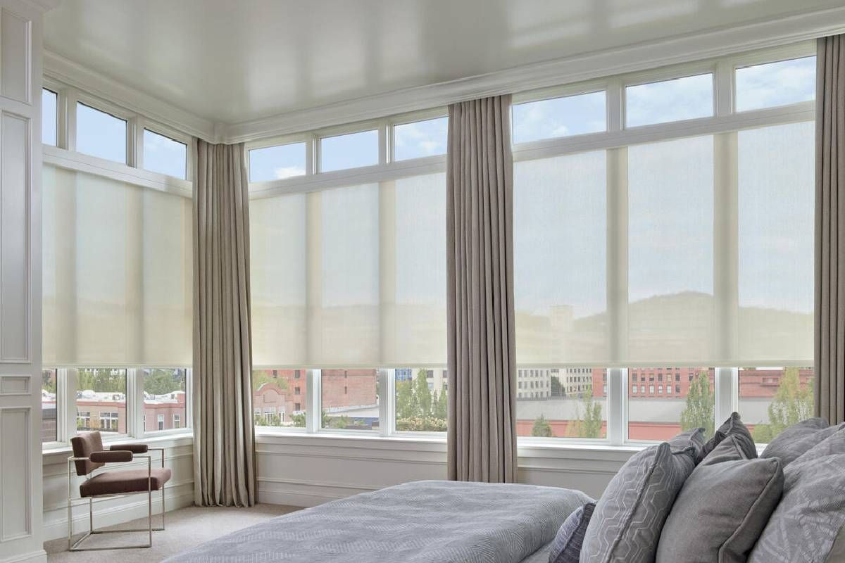 A bedroom with a bed , chair , and lots of Hunter Douglas treated windows.