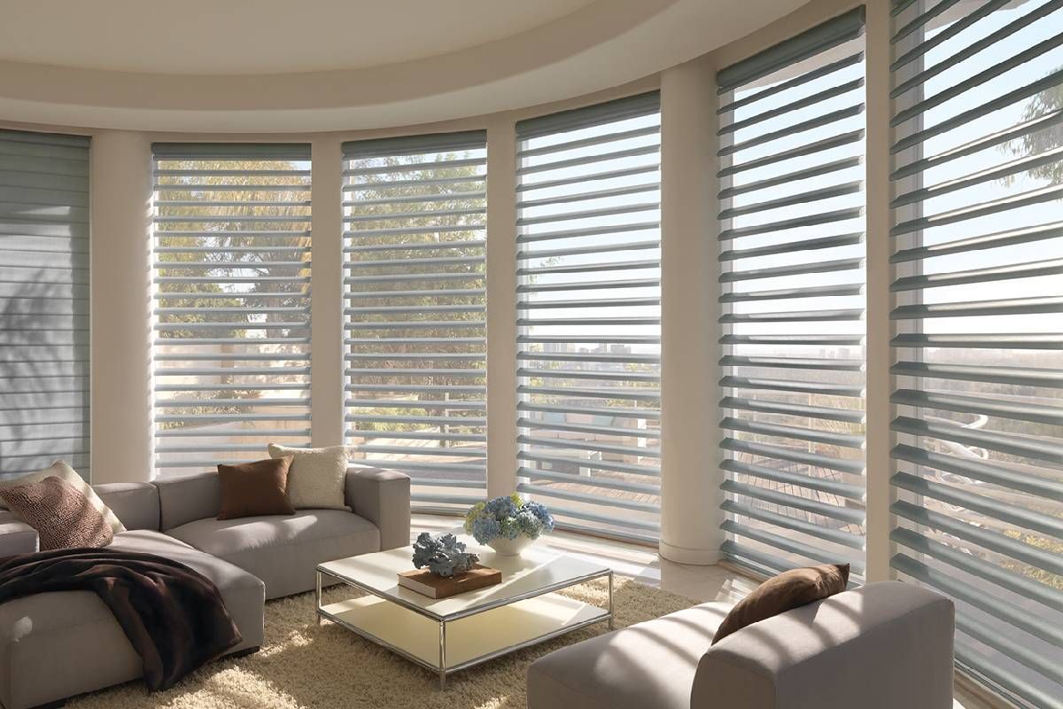 A living room with a couch , chairs , and a coffee table in front of Hunter Douglas shutters