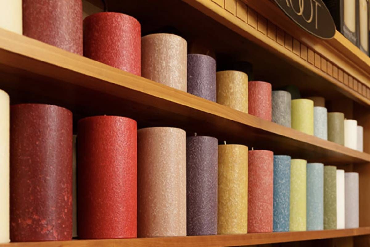 Many different colored candles are lined up on a wooden shelf to decorate a home