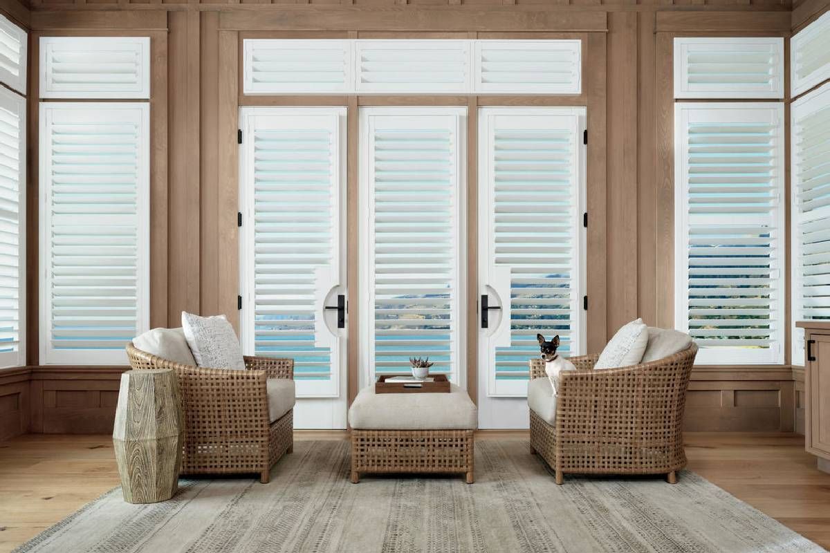 A living room with two wicker chairs and a table with shutters on the Hunter Douglas treated windows.