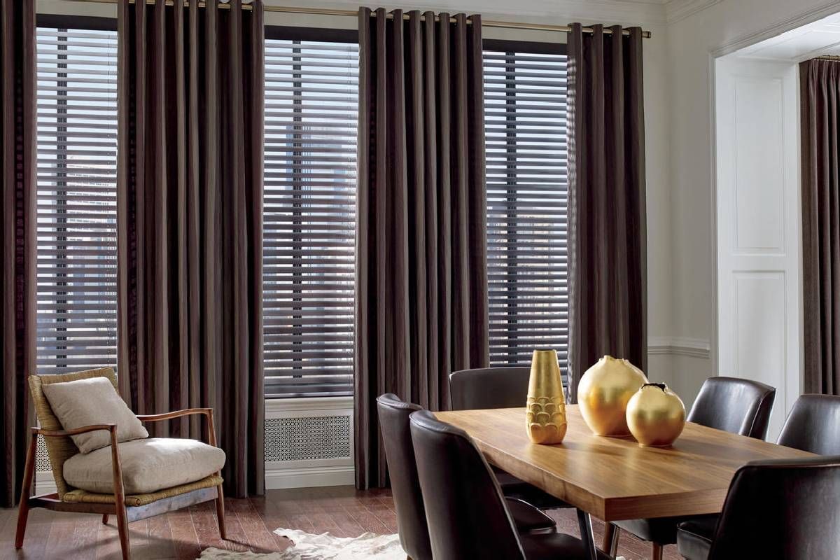 A dining room with a table , chairs , vases and curtains on a Hunter Douglas treated window