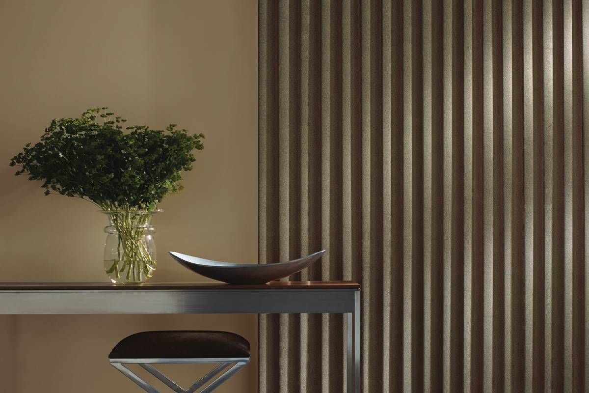 A vase of flowers is sitting on a table in front of a wall with vertical blinds on a Hunter Douglas treated window