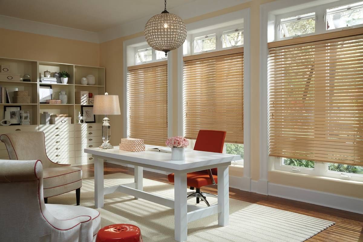 A living room with a desk , chairs , and blinds on the Hunter Douglas treated windows.