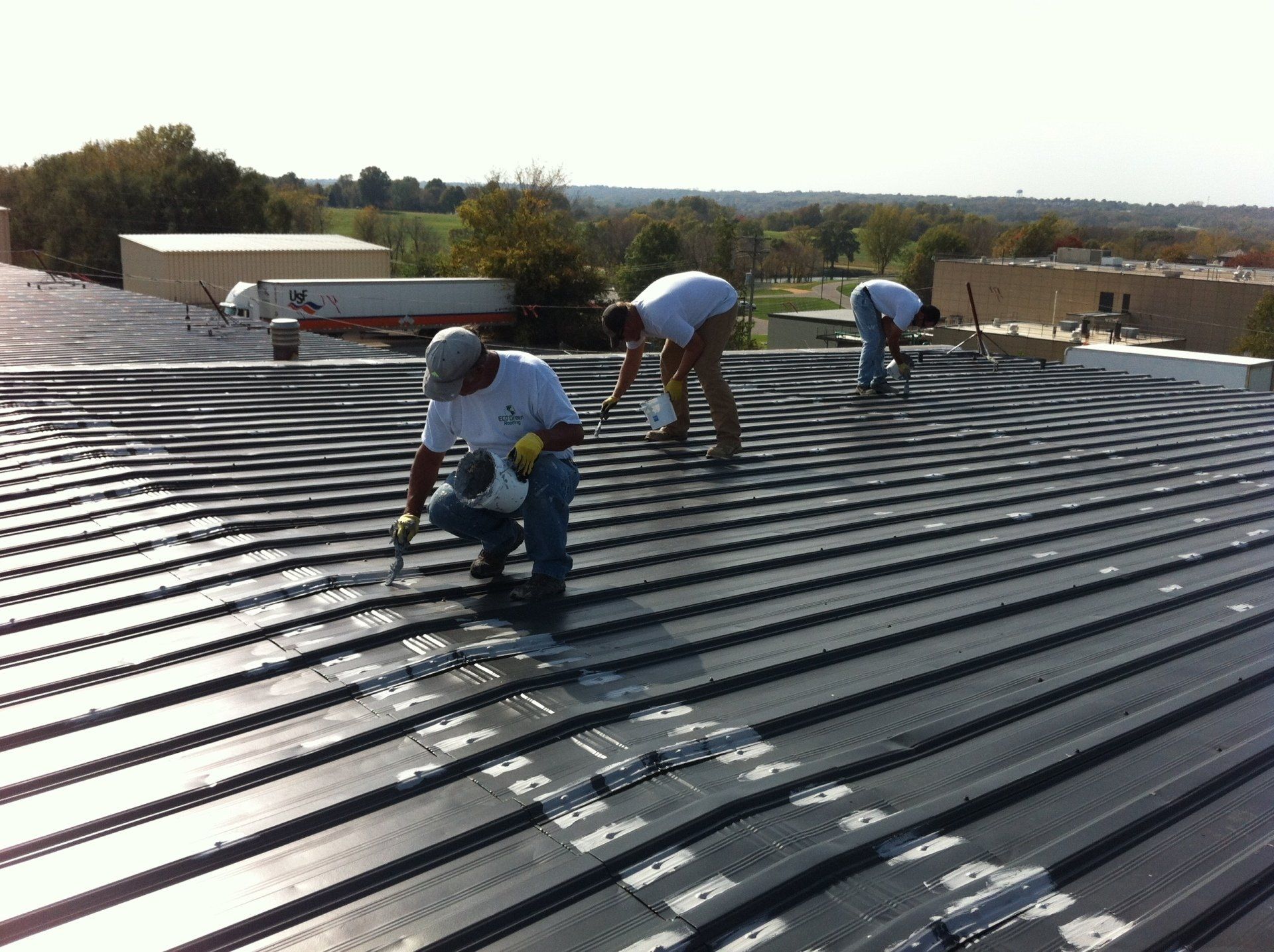 Three men are working on the roof of a metal building