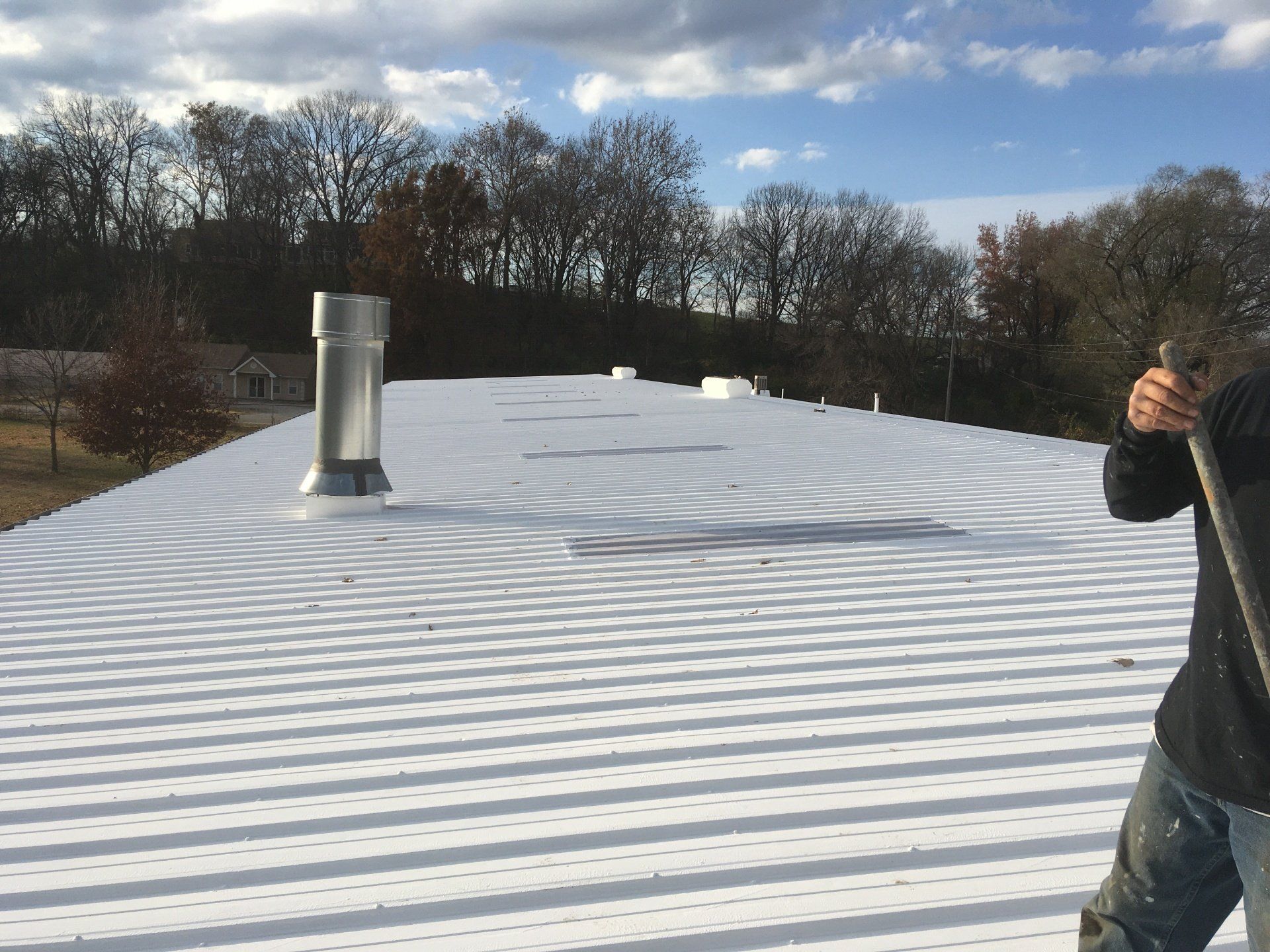 A man is standing on a white roof with trees in the background.