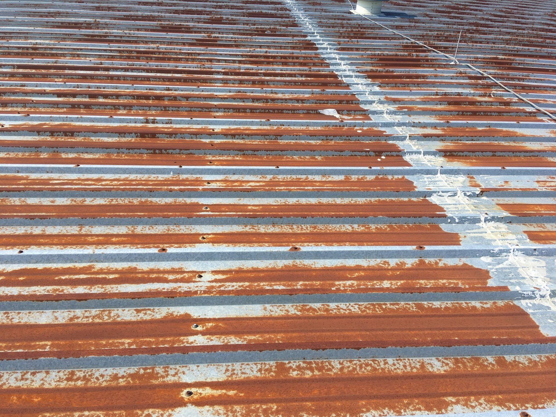 A rusty metal roof being repaired and prepped for a protective coating.